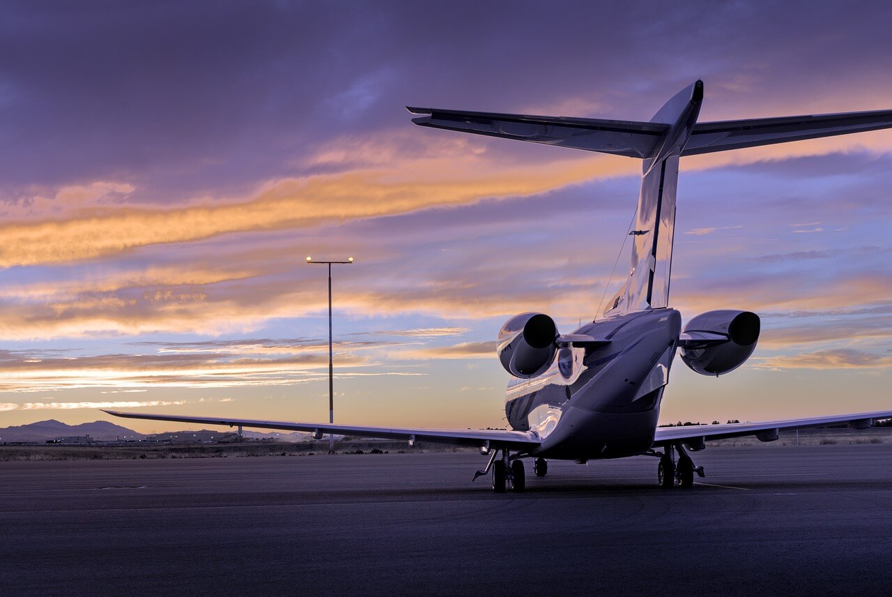 A jet airplane on the airport tarmac, parked with a sunset behind.