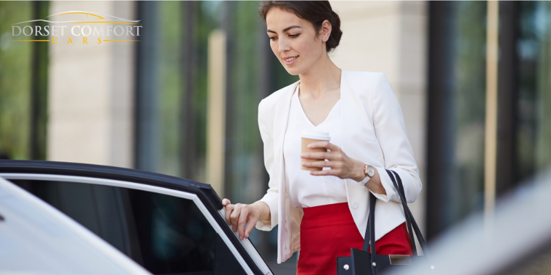 A happy businesswoman carrying a cup of coffee getting into the back of a car.